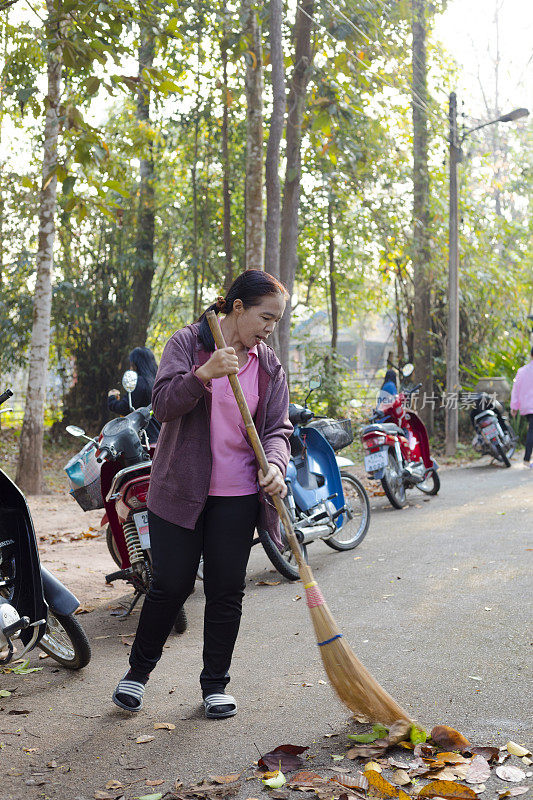 一名成熟的泰国妇女在Phu Langka国家公园用扫帚清理道路上的树叶